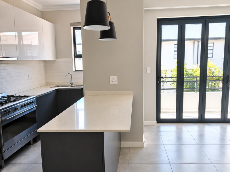 Modern kitchen featuring sleek cabinetry, stone countertops, a central island, and bi-fold doors leading to an outdoor area.