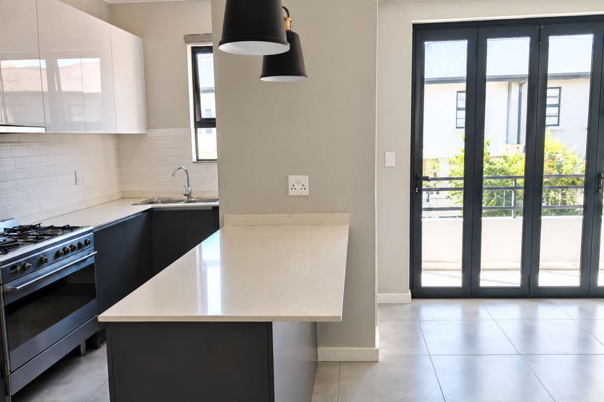 Modern kitchen featuring sleek cabinetry, stone countertops, a central island, and bi-fold doors leading to an outdoor area.
