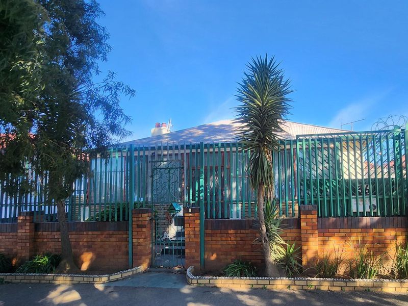 Front elevation of a residential property featuring a brick boundary wall, metal security fencing, and a tiled roof structure.