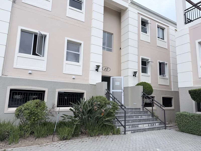 Front elevation of a multi-story office building featuring a paved entrance, tiled staircase with metal handrails, and well-maintained exterior facade.