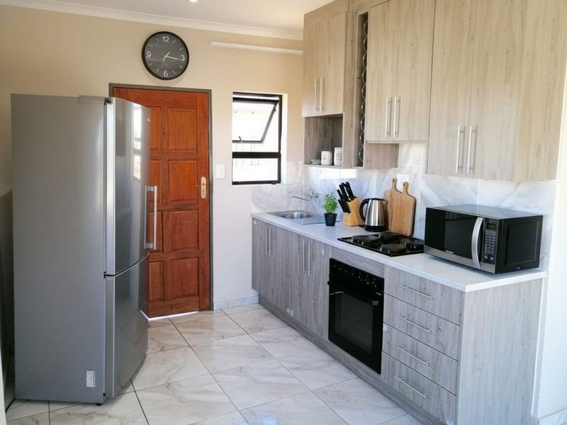 Modern kitchen featuring light wood-grain cabinetry, stone countertops, built-in oven, gas hob, and tiled flooring with direct access to an exterior door.