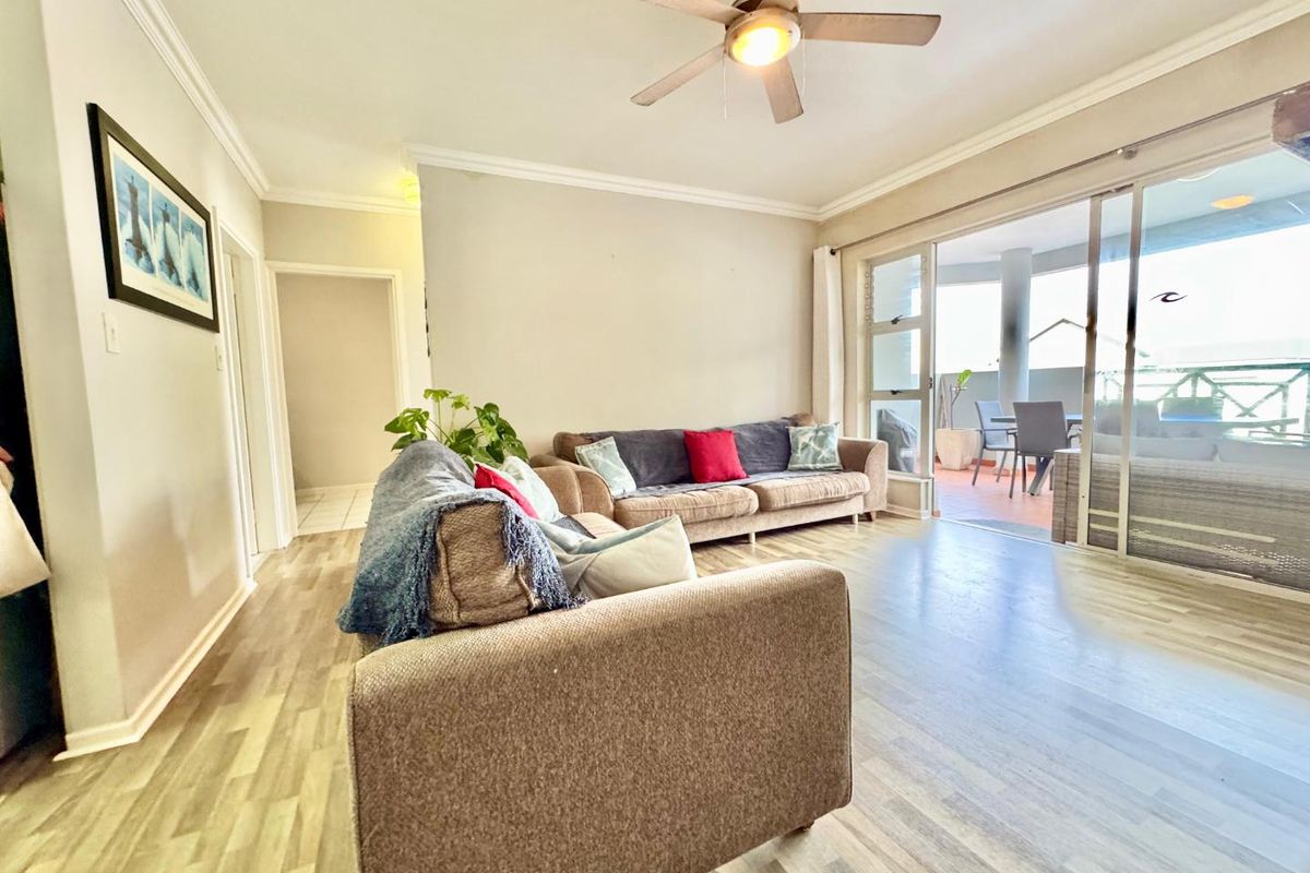 Spacious living room featuring wood-look flooring, crown molding, a ceiling fan, and large sliding glass doors providing seamless access to the outdoor patio area.