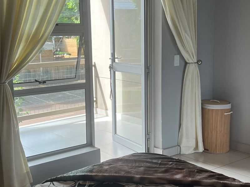 A bedroom featuring tiled flooring and direct access to a private balcony through an aluminium framed glass door.