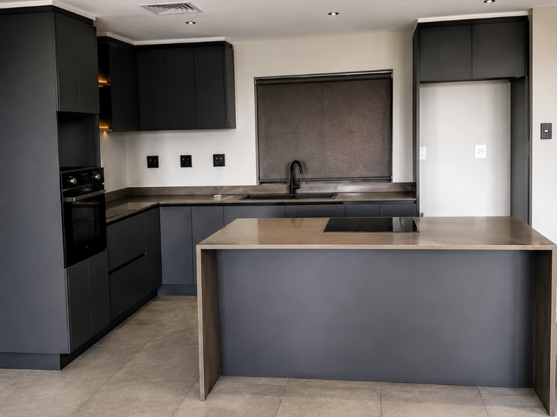Modern kitchen featuring dark cabinetry, a central island with an integrated hob, stone countertops, and high-quality built-in appliances in a spacious, minimalist layout.
