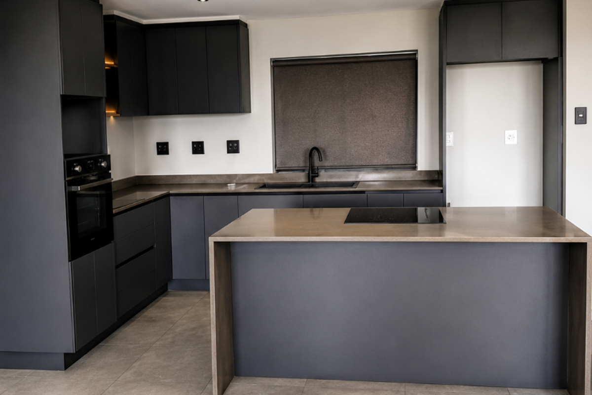 Modern kitchen featuring dark cabinetry, a central island with an integrated hob, stone countertops, and high-quality built-in appliances in a spacious, minimalist layout.