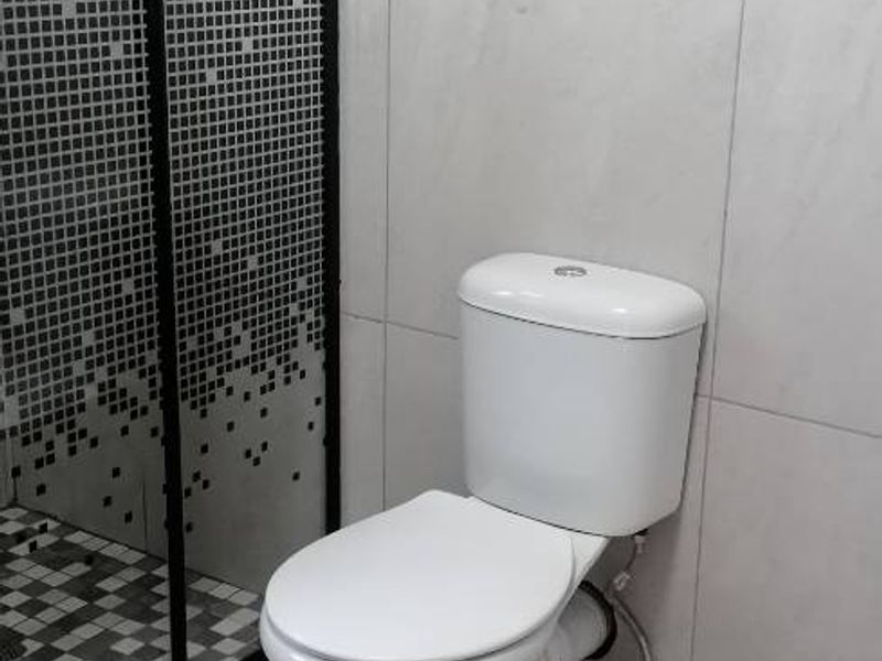 A modern bathroom featuring a glass-enclosed shower with patterned detailing and a standard white toilet, finished with neutral floor and wall tiles.