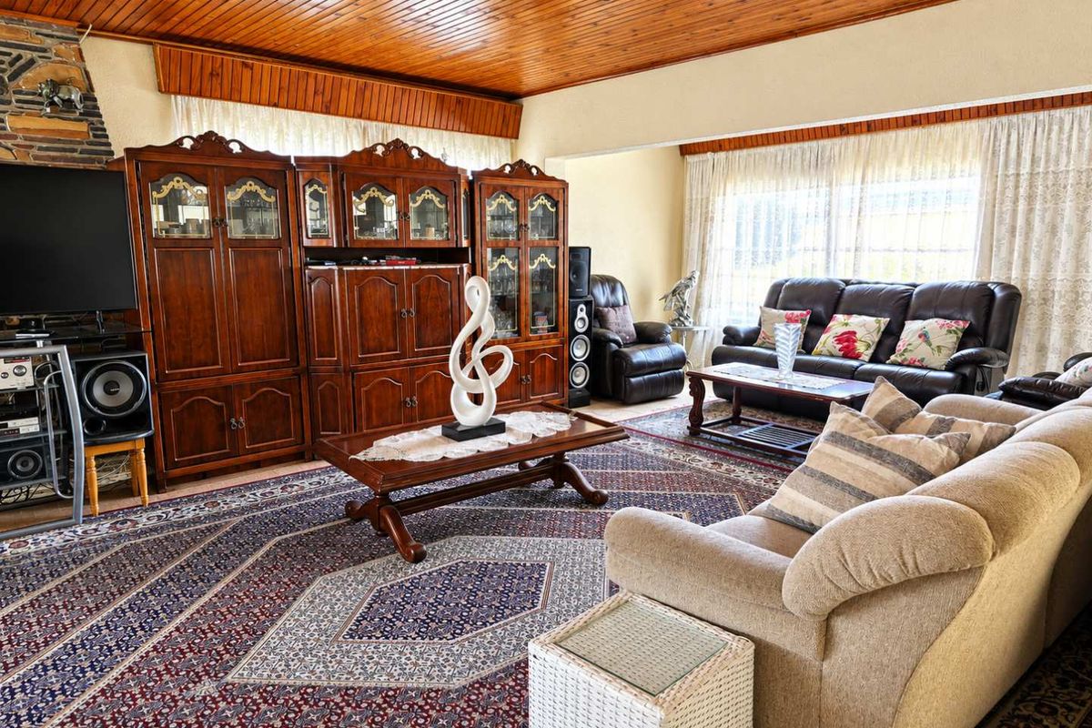 A spacious living room featuring a distinctive timber tongue and groove ceiling and a stone-clad fireplace surround, offering a warm and traditional aesthetic.