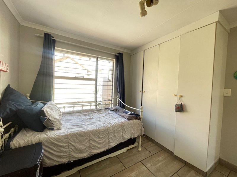 A functional bedroom featuring tiled flooring, built-in cupboards for storage, and a window fitted with security burglar bars.