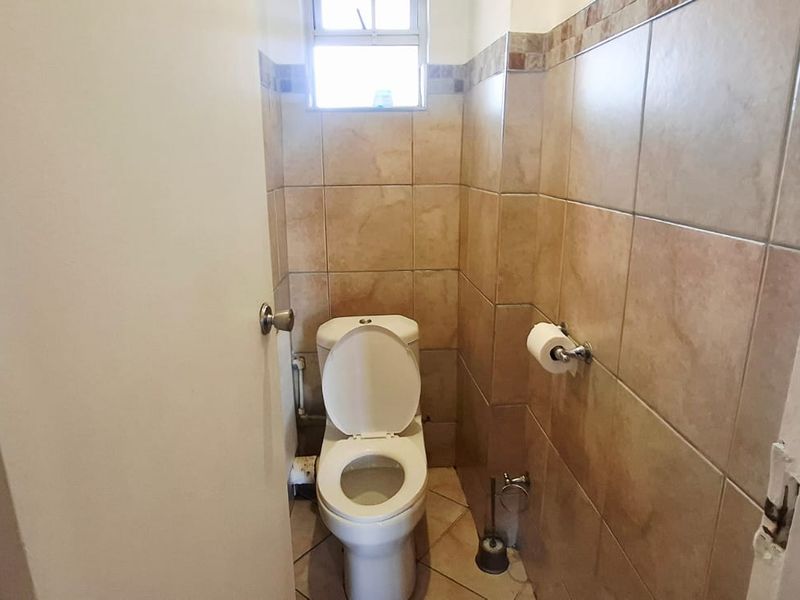 A compact bathroom featuring tiled walls and flooring, equipped with a standard toilet and a small window for ventilation.