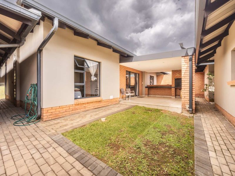 Rear exterior view of the townhouse featuring a covered patio with a built-in braai, brick paving, and a small garden area.