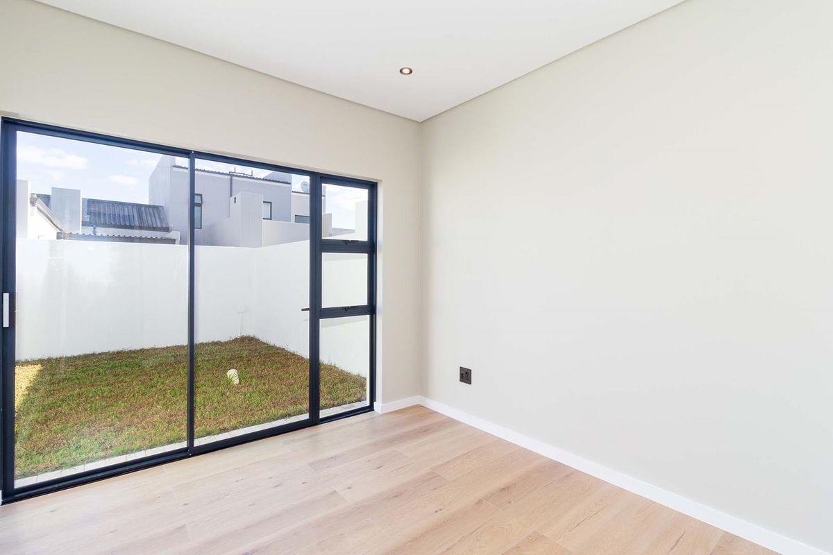 A bright, modern bedroom featuring light wood-look flooring, neutral walls, and large black-framed sliding glass doors providing direct access to a private rear garden.