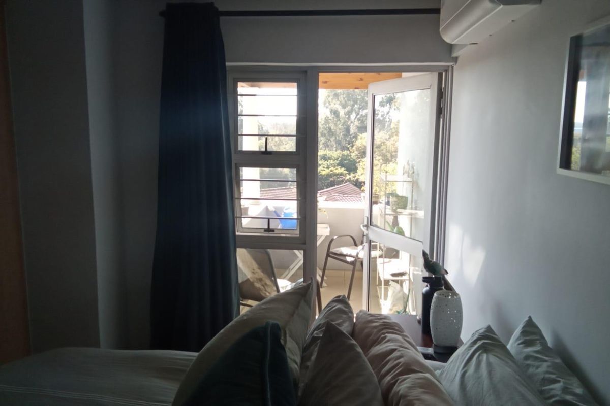 A bedroom featuring a wall-mounted air conditioning unit and a glass door providing direct access to a private balcony.