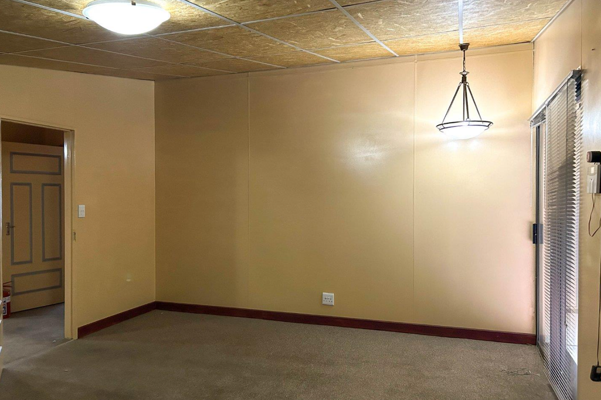 An empty living room featuring carpet flooring, a sliding glass door with blinds, and a suspended ceiling with integrated lighting fixtures.