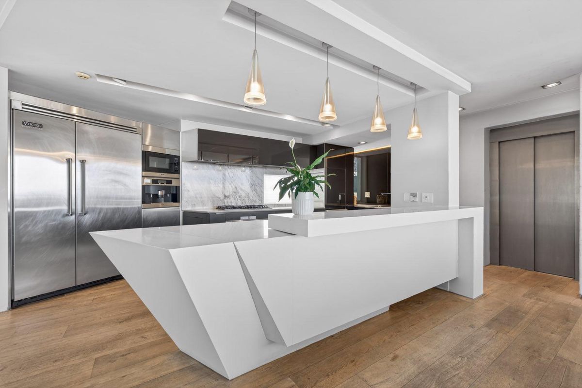 Modern kitchen featuring a large sculptural island, premium stone countertops, high-end built-in stainless steel appliances, and elegant pendant lighting over hardwood floors.