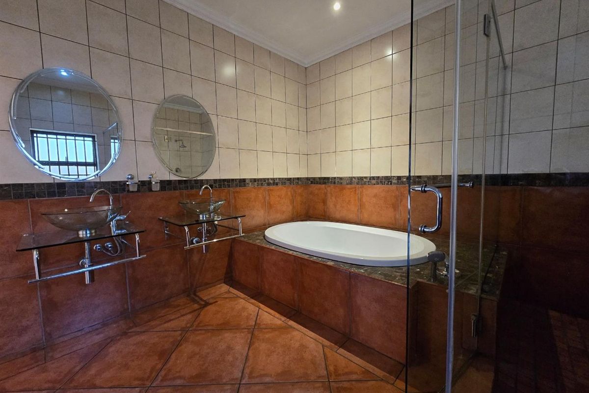 Spacious bathroom featuring a built-in bathtub, glass-enclosed shower, and dual glass vessel sinks with wall-mounted mirrors.