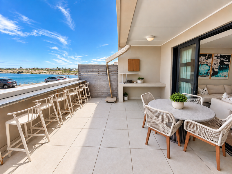 Spacious covered balcony featuring tiled flooring, a built-in stone counter, and sliding glass doors, offering expansive waterfront views.