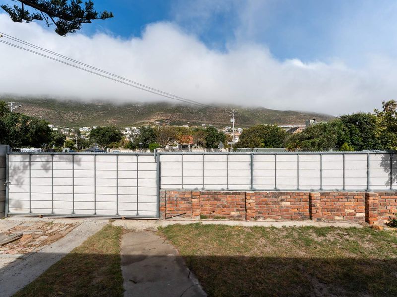 Front exterior view featuring a sliding metal gate, brick boundary wall, and concrete driveway with mountain views in the background.