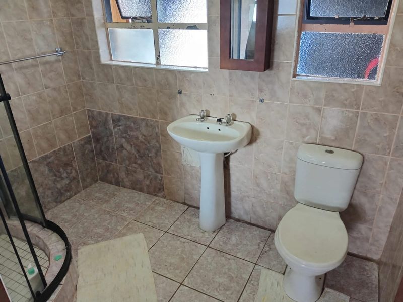 A dated bathroom featuring a pedestal basin, toilet, and shower enclosure with tiled finishes throughout, requiring cosmetic updates to modernize the space.