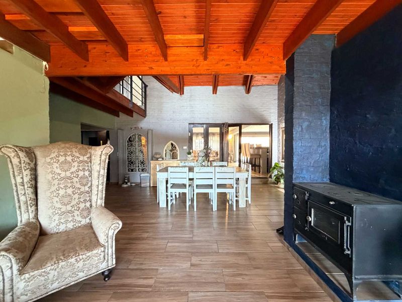 Spacious open-plan living and dining area featuring exposed timber ceiling beams, a prominent brick fireplace with a wood-burning stove, and tiled flooring.