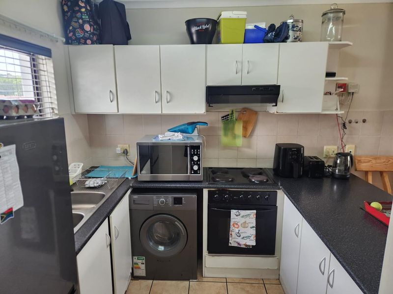 Compact kitchen featuring white cabinetry, dark laminate countertops, built-in oven with hob, extractor fan, and tiled backsplash.