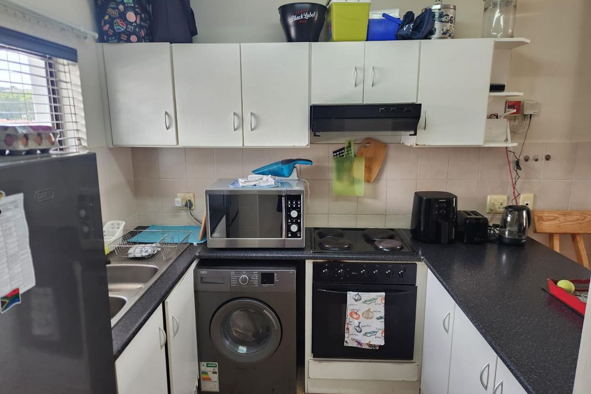 Compact kitchen featuring white cabinetry, dark laminate countertops, built-in oven with hob, extractor fan, and tiled backsplash.