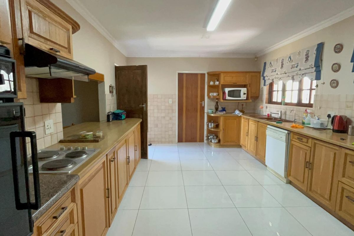 Spacious kitchen featuring extensive wooden cabinetry, tiled flooring, built-in oven and hob, and ample counter space for meal preparation.