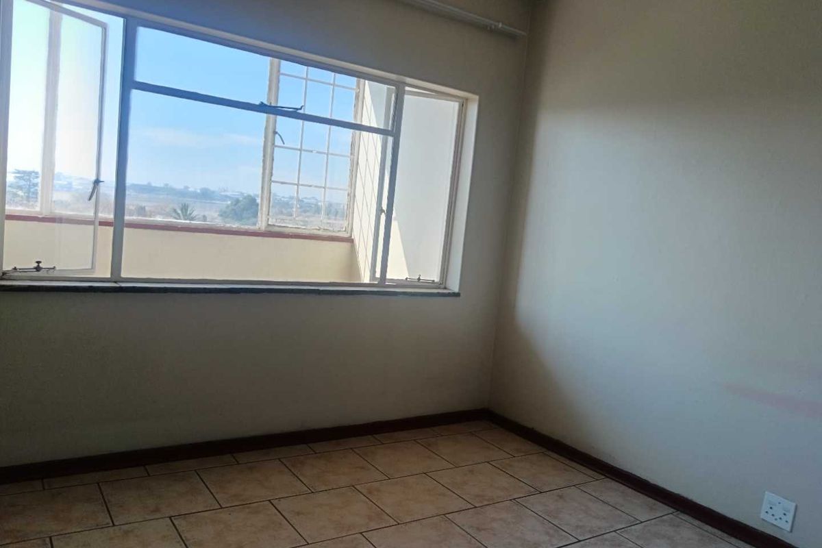 An empty bedroom featuring tiled flooring and a large window with natural light, ready for personalization.