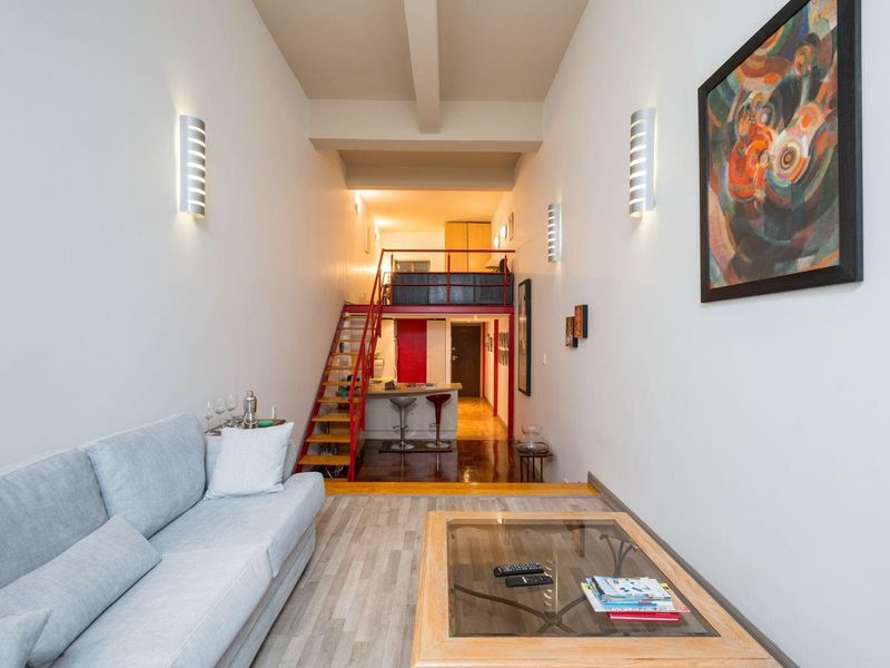 Open-plan living area featuring a mezzanine level, metal staircase, and a kitchen island with integrated finishes, creating a modern loft-style apartment layout.