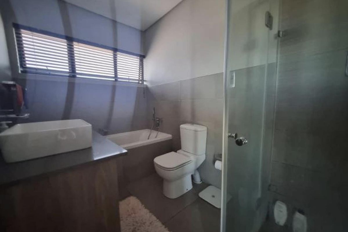 A modern bathroom featuring a glass-enclosed shower, a separate bathtub, a vanity with a vessel sink, and neutral wall tiling.