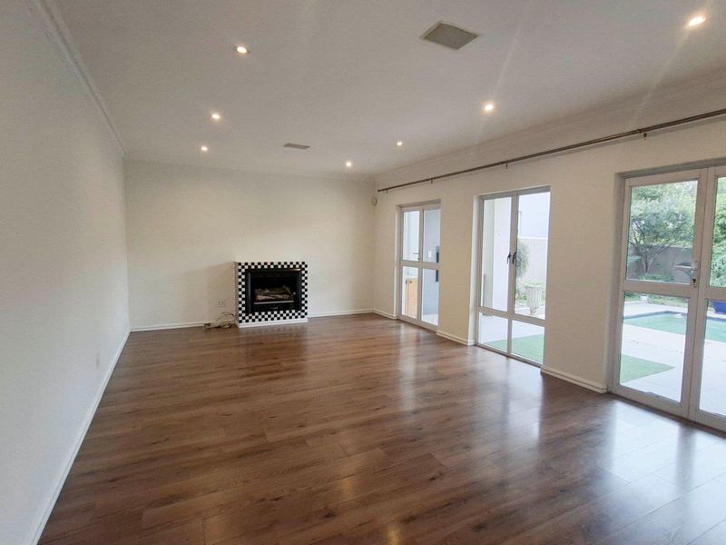 Spacious living room featuring laminate flooring, a built-in fireplace, and large glass doors providing direct access to the outdoor pool area.