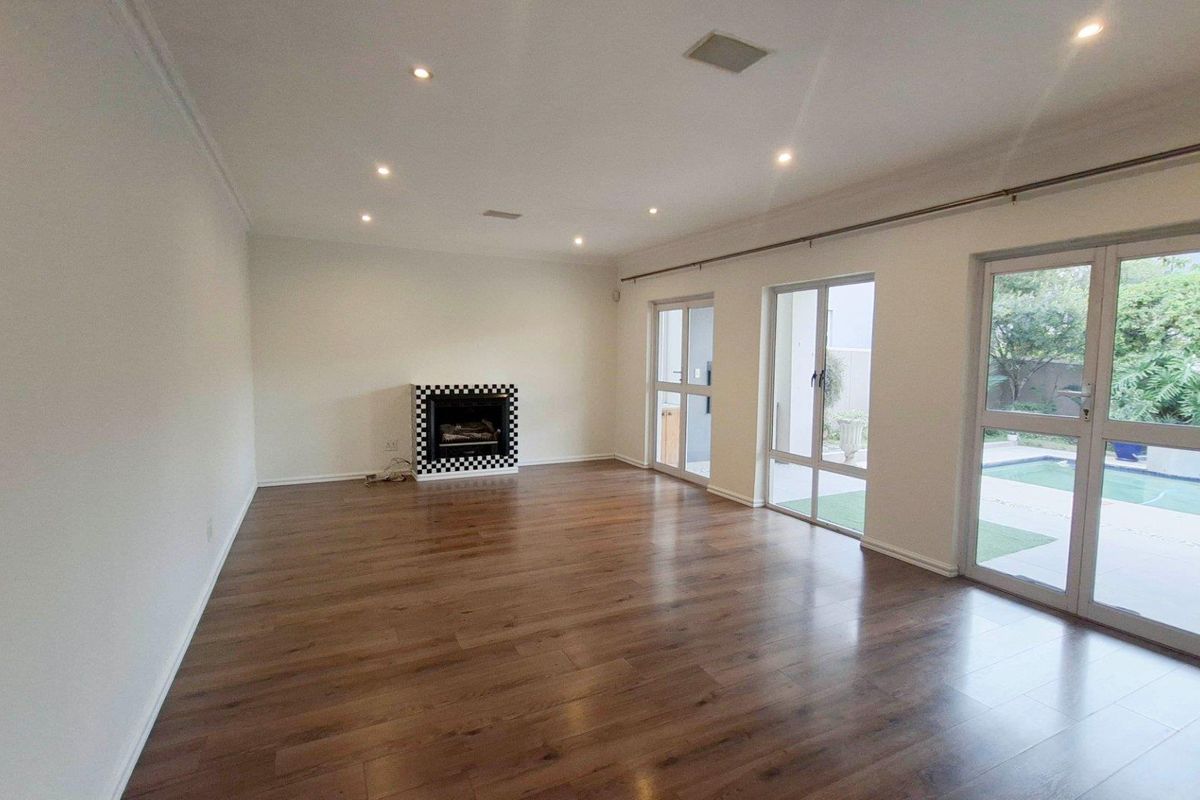 Spacious living room featuring laminate flooring, a built-in fireplace, and large glass doors providing direct access to the outdoor pool area.