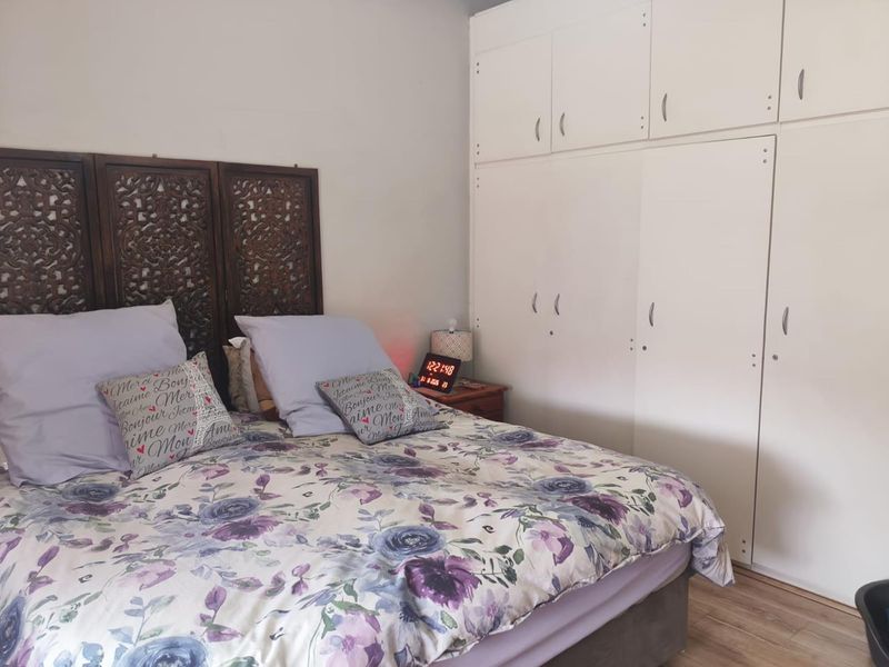 A bedroom featuring built-in white cupboards and laminate flooring, providing functional storage space.