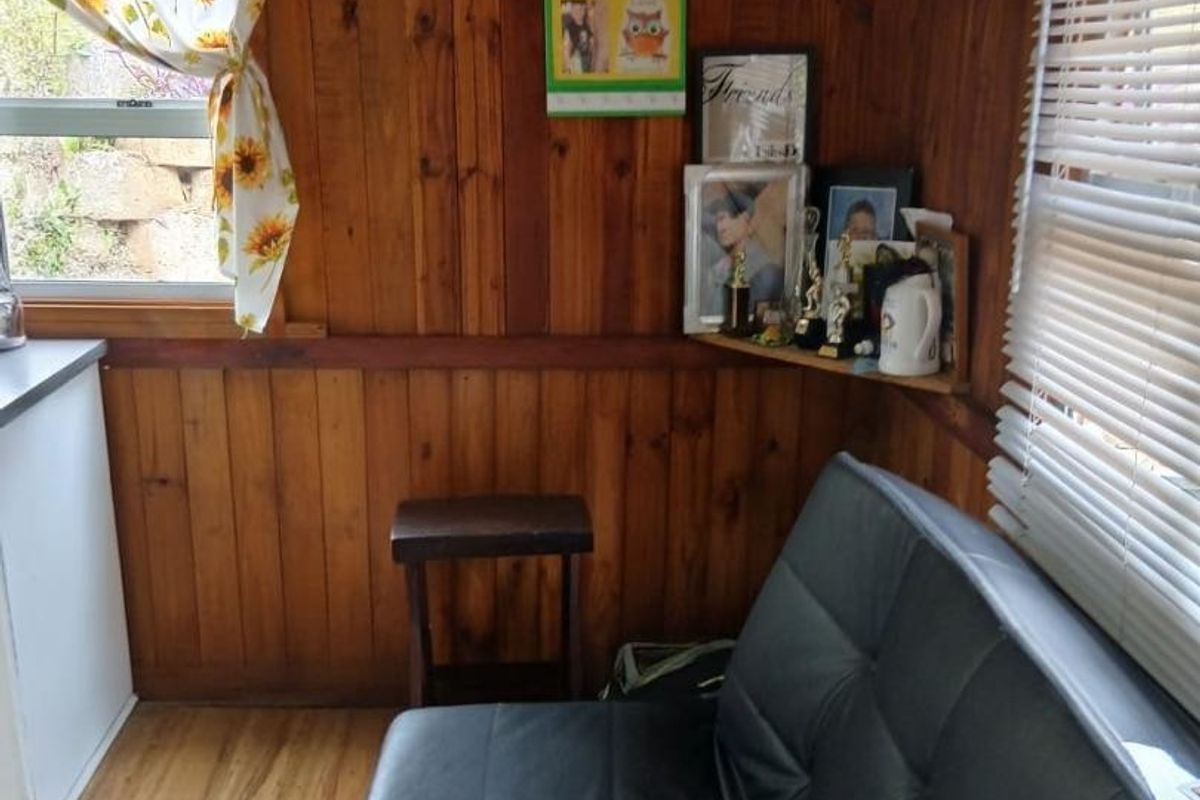 A cozy living space featuring warm timber wall paneling, laminate flooring, and natural light through venetian blinds.