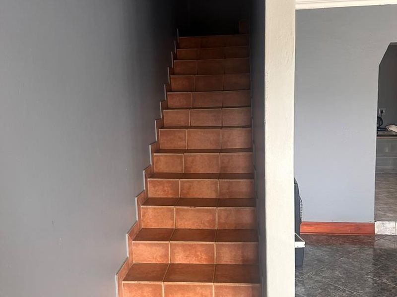 A functional hallway featuring a tiled staircase and tiled flooring, leading to an adjacent living area with grey painted walls.