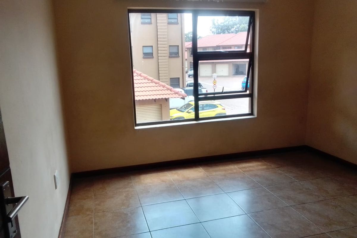 An empty bedroom featuring tiled flooring and a window with views of the surrounding apartment complex.