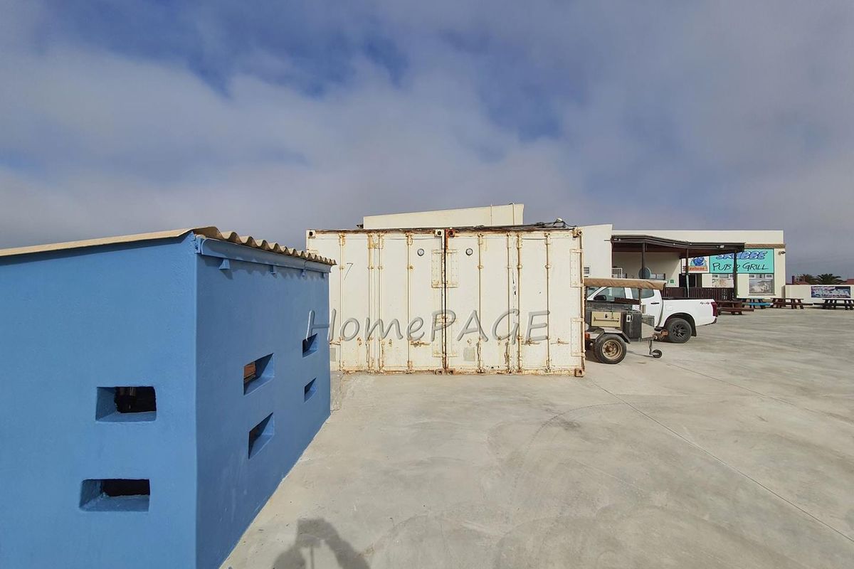 Exterior view of a commercial property featuring a blue utility structure, a large shipping container, and expansive concrete paved area.