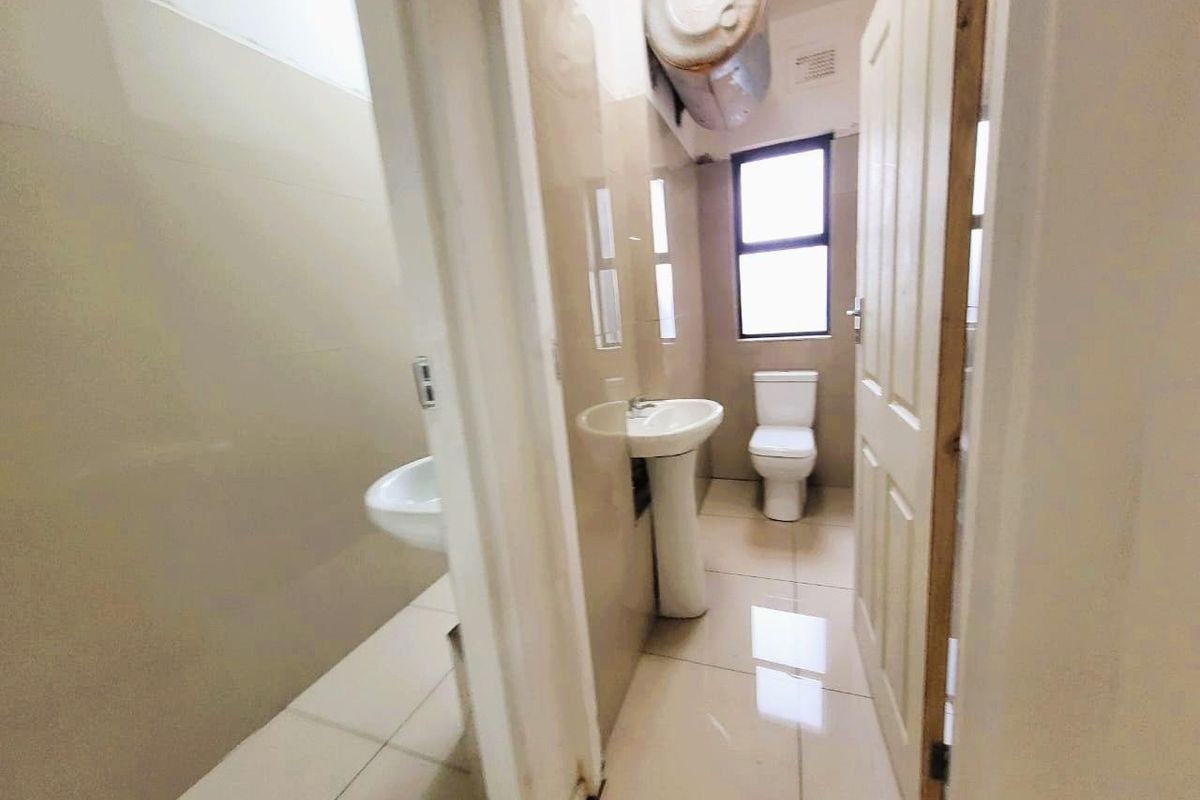 A functional bathroom featuring tiled walls and flooring, a pedestal basin, and a toilet, with an exposed water heater unit.