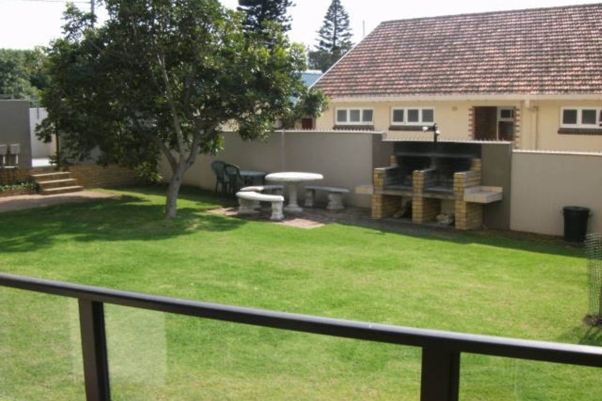 A private rear garden featuring a built-in brick braai area, manicured lawn, and perimeter boundary wall, viewed from an elevated balcony.