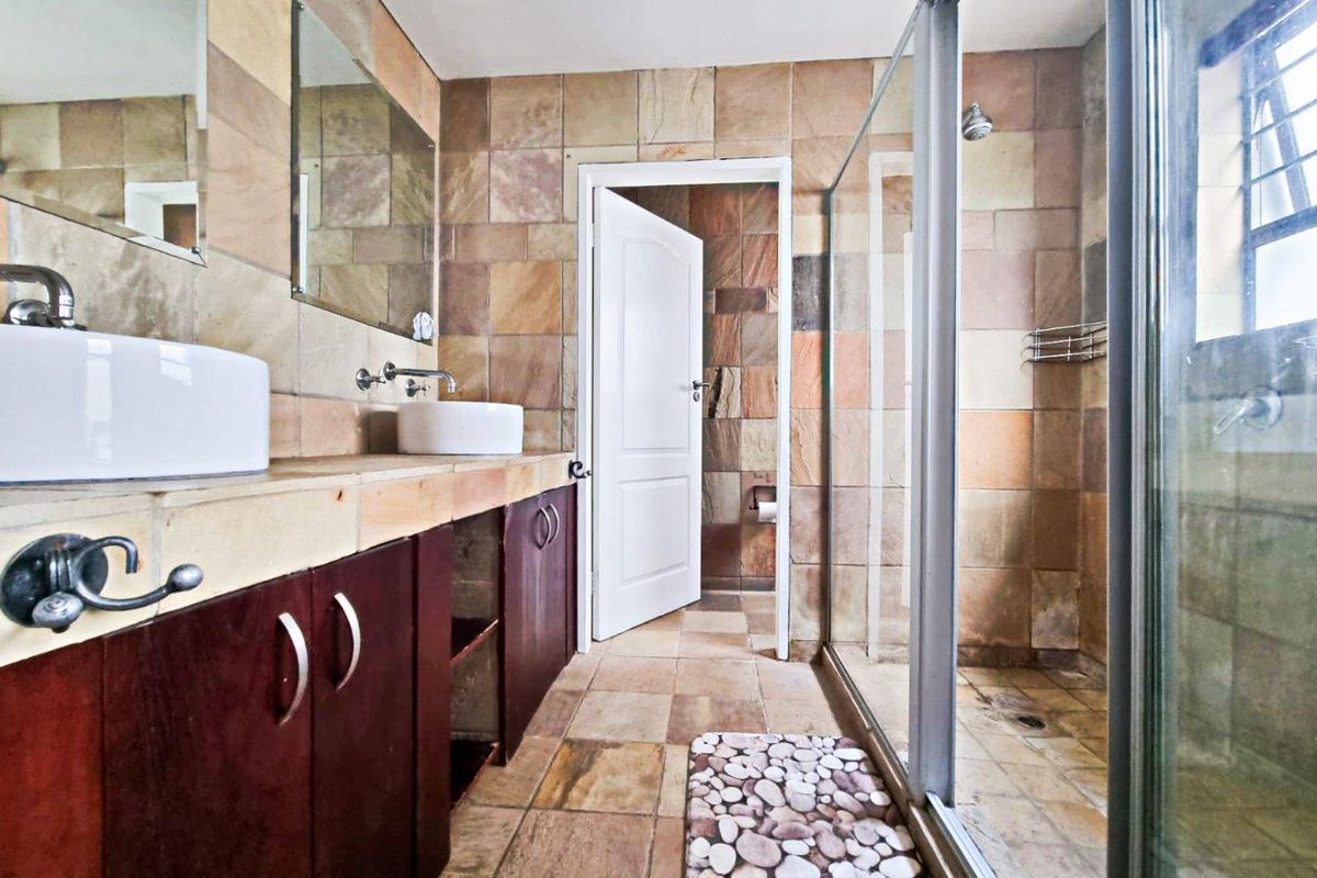A bathroom featuring a double vanity with vessel sinks, stone wall and floor tiles, and a glass-enclosed walk-in shower.