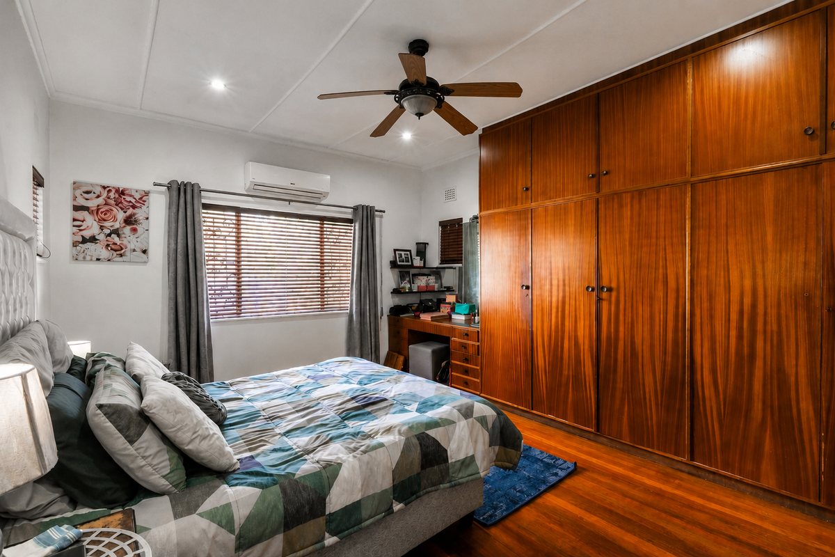 A well-maintained bedroom featuring polished hardwood floors, extensive built-in wooden cabinetry, a ceiling fan, and a wall-mounted air conditioning unit.