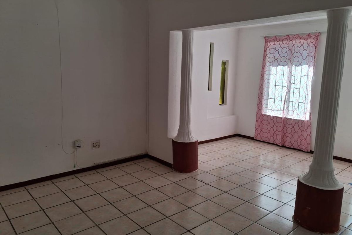 An empty living area featuring tiled flooring, decorative columns, and vertical accent windows, offering a blank canvas for renovation.