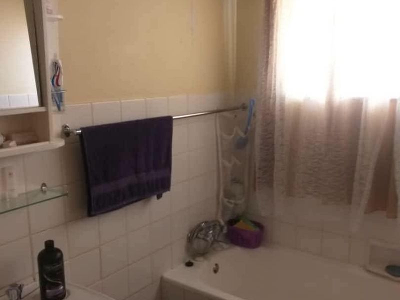 A dated bathroom featuring a built-in bathtub, wall-mounted basin, and tiled splashback, currently showing signs of wear and wall surface deterioration.