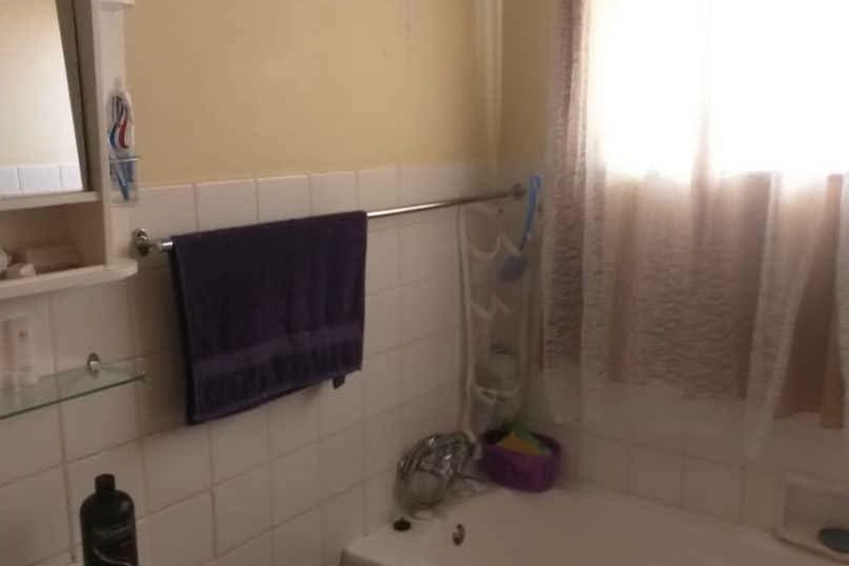 A dated bathroom featuring a built-in bathtub, wall-mounted basin, and tiled splashback, currently showing signs of wear and wall surface deterioration.