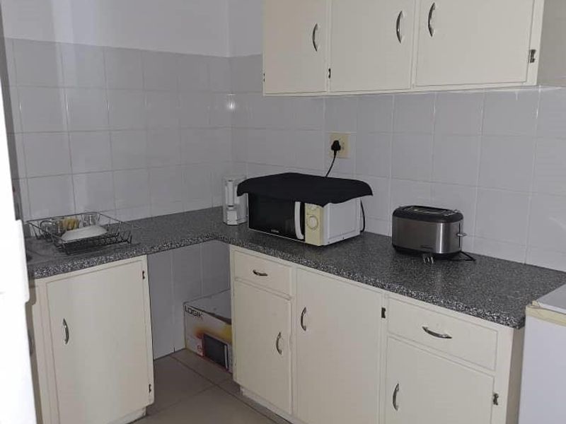 A functional kitchen area featuring built-in cabinetry, laminate countertops, and a tiled backsplash, providing a practical workspace for office staff.