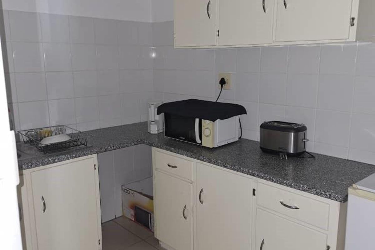 A functional kitchen area featuring built-in cabinetry, laminate countertops, and a tiled backsplash, providing a practical workspace for office staff.