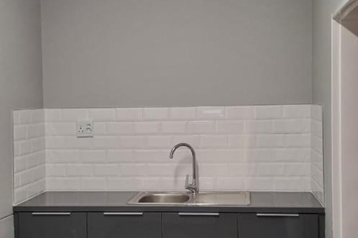A clean, modern kitchenette featuring dark grey cabinetry, a stainless steel sink, and a white subway tile backsplash in a well-lit office space.
