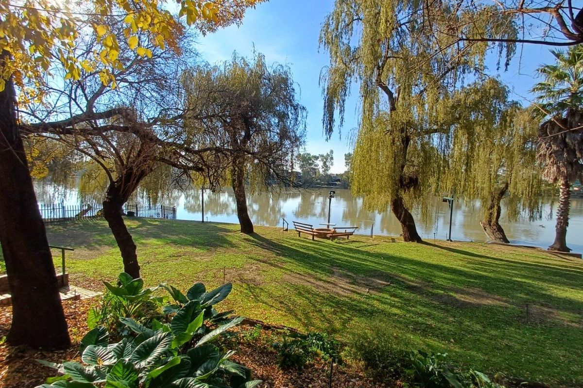 A scenic garden area featuring mature willow trees and direct access to a riverfront, offering a peaceful outdoor setting.
