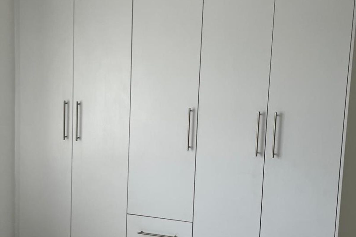 A bedroom featuring floor-to-ceiling built-in white cabinetry with modern metal handles and tiled flooring.