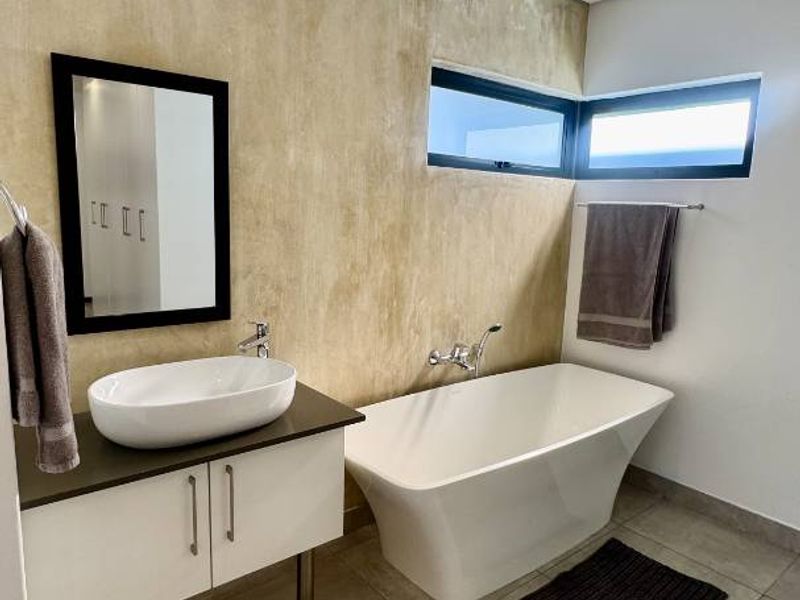 Modern bathroom featuring a sleek freestanding bathtub, vessel sink vanity, and contemporary wall finishes with large format floor tiles.