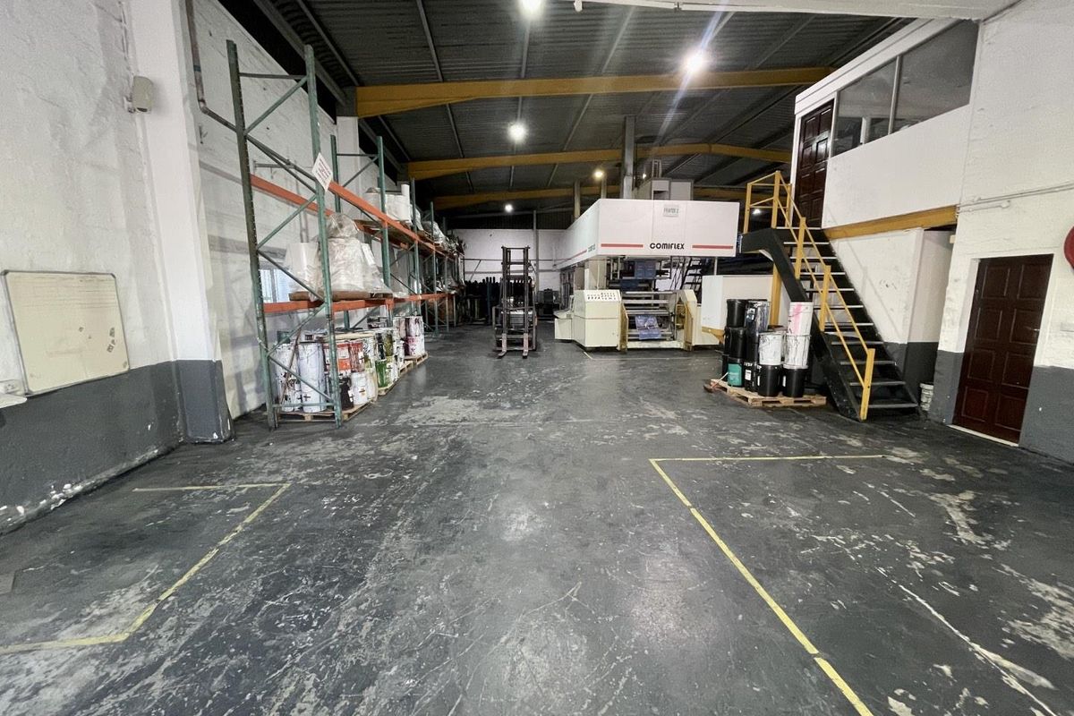 Spacious industrial warehouse area featuring high ceilings with exposed steel trusses, mezzanine access, and durable flooring suitable for manufacturing or storage operations.
